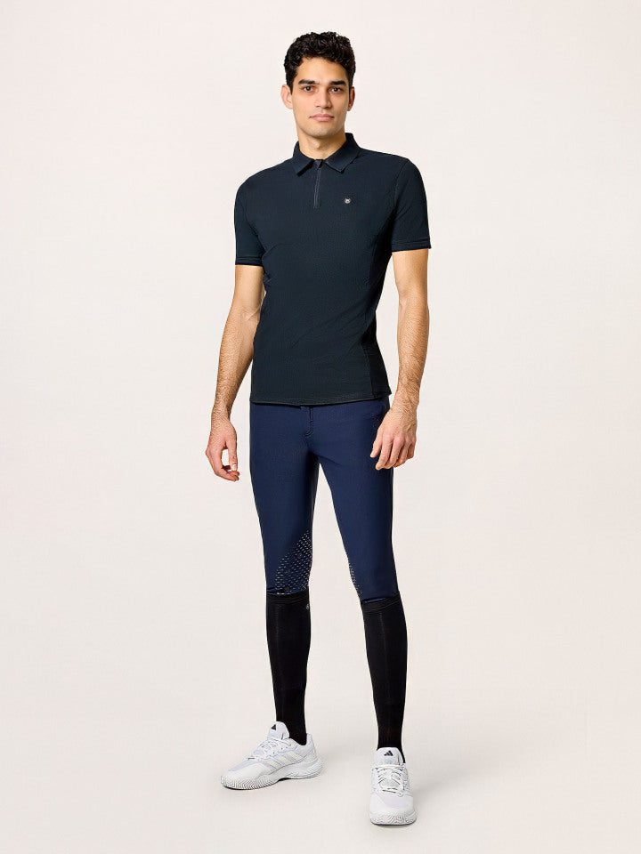 A model wearing Equestrian Stockholm Polo Shirt Zip Men Black with navy breeches and white sneakers.