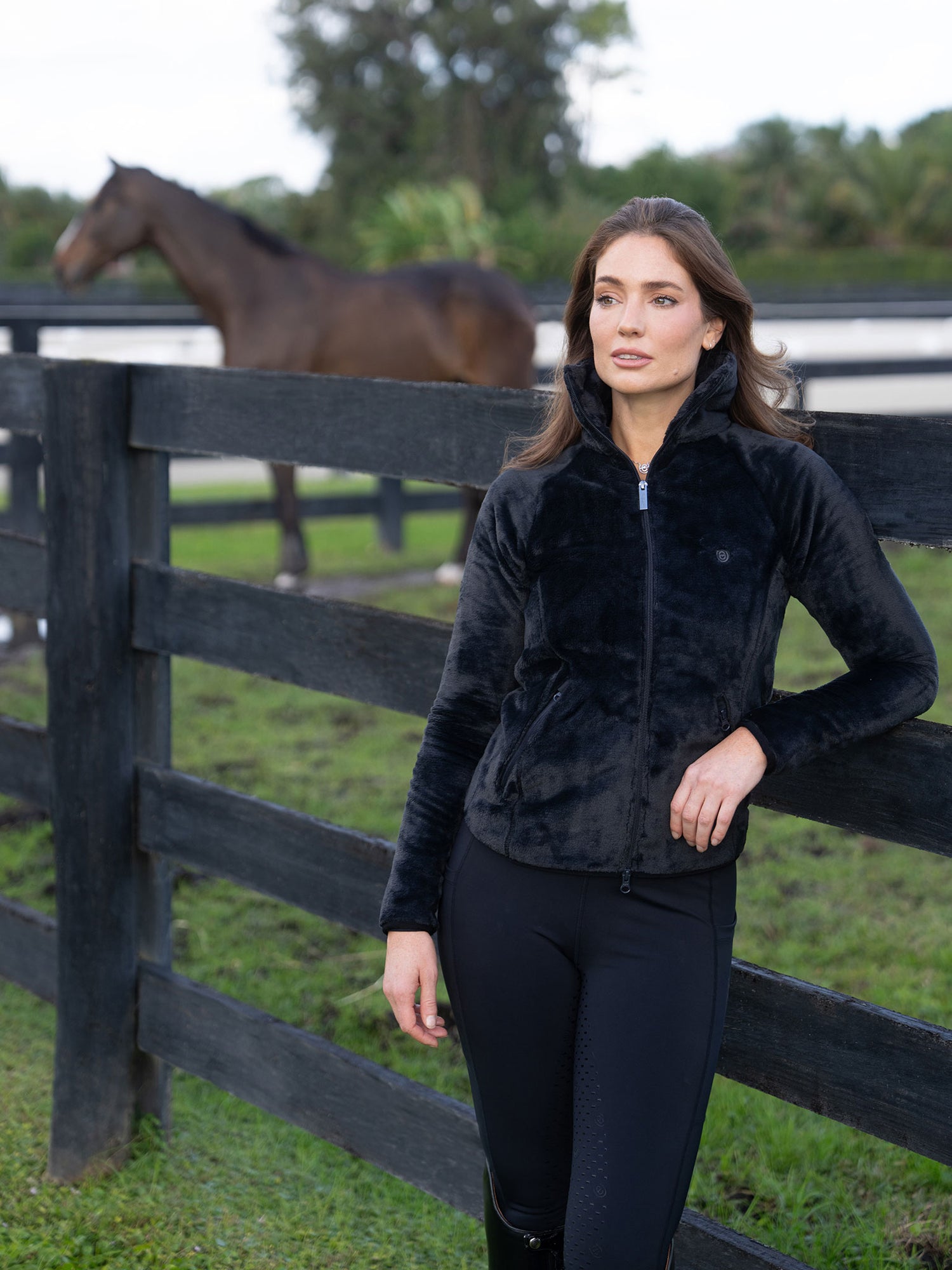 Mannequin en veste polaire Equestrian Stockholm Velvet Black appuyée contre une clôture avec un cheval.
