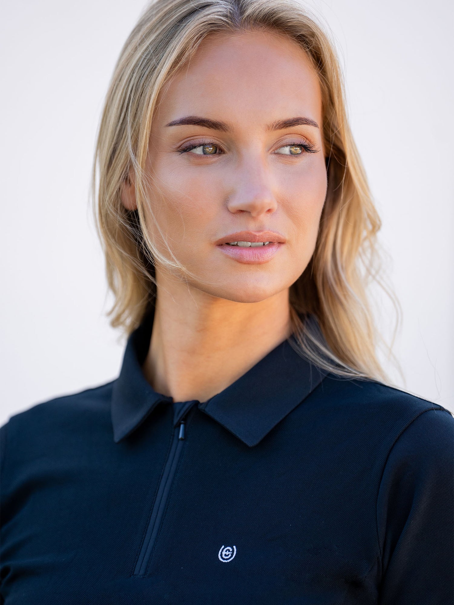 Blonde model wearing the black Equestrian Stockholm Polo Shirt Zip featuring a quarter-zip and small chest logo.