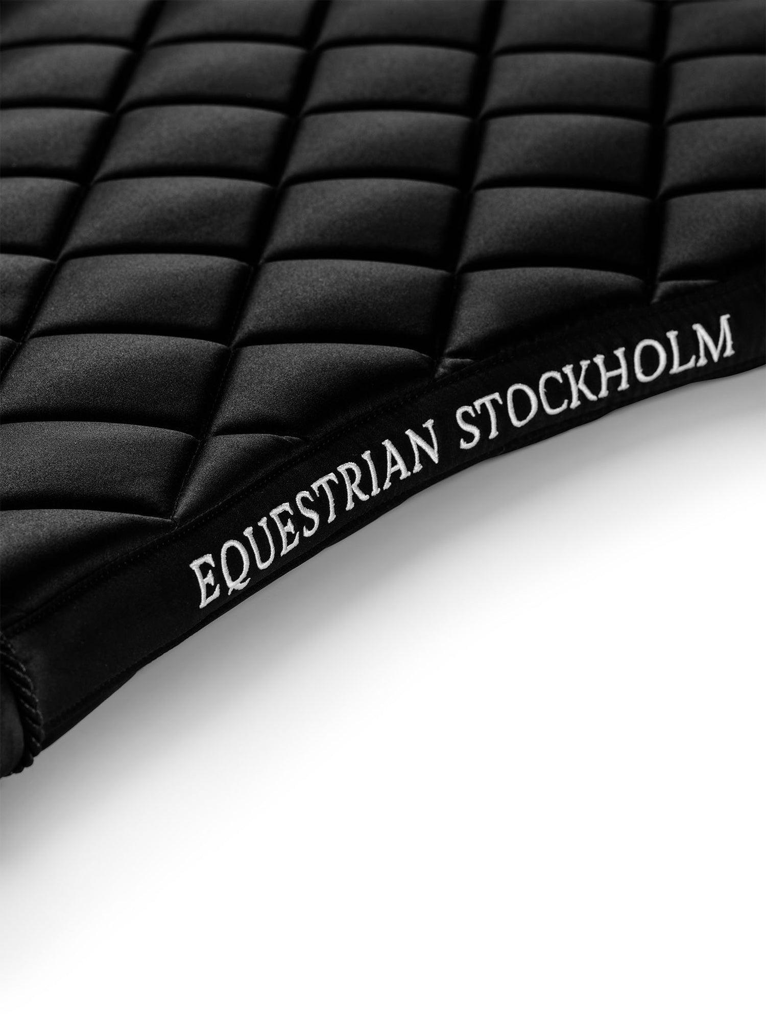 Studiobillede af Equestrian Stockholm dressurunderlag Line Black med hvidt broderi og firkantet quiltning.