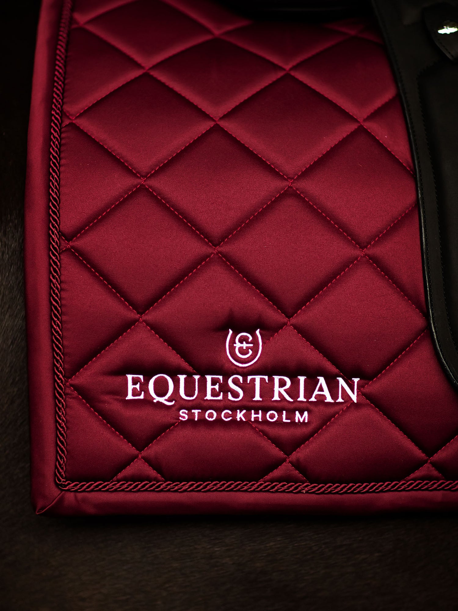 Studio image of Equestrian Stockholm Dressage Saddle Pad Line Bordeaux featuring white logo embroidery and rope piping.