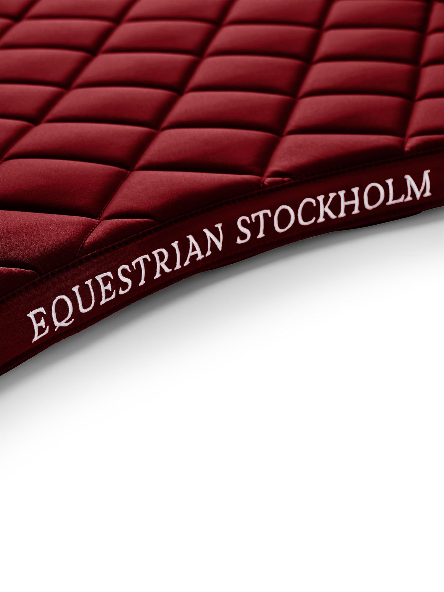 Studiobillede af Equestrian Stockholm Line Bordeaux sadelunderlag med hvidt logobroderi og line-quiltning.