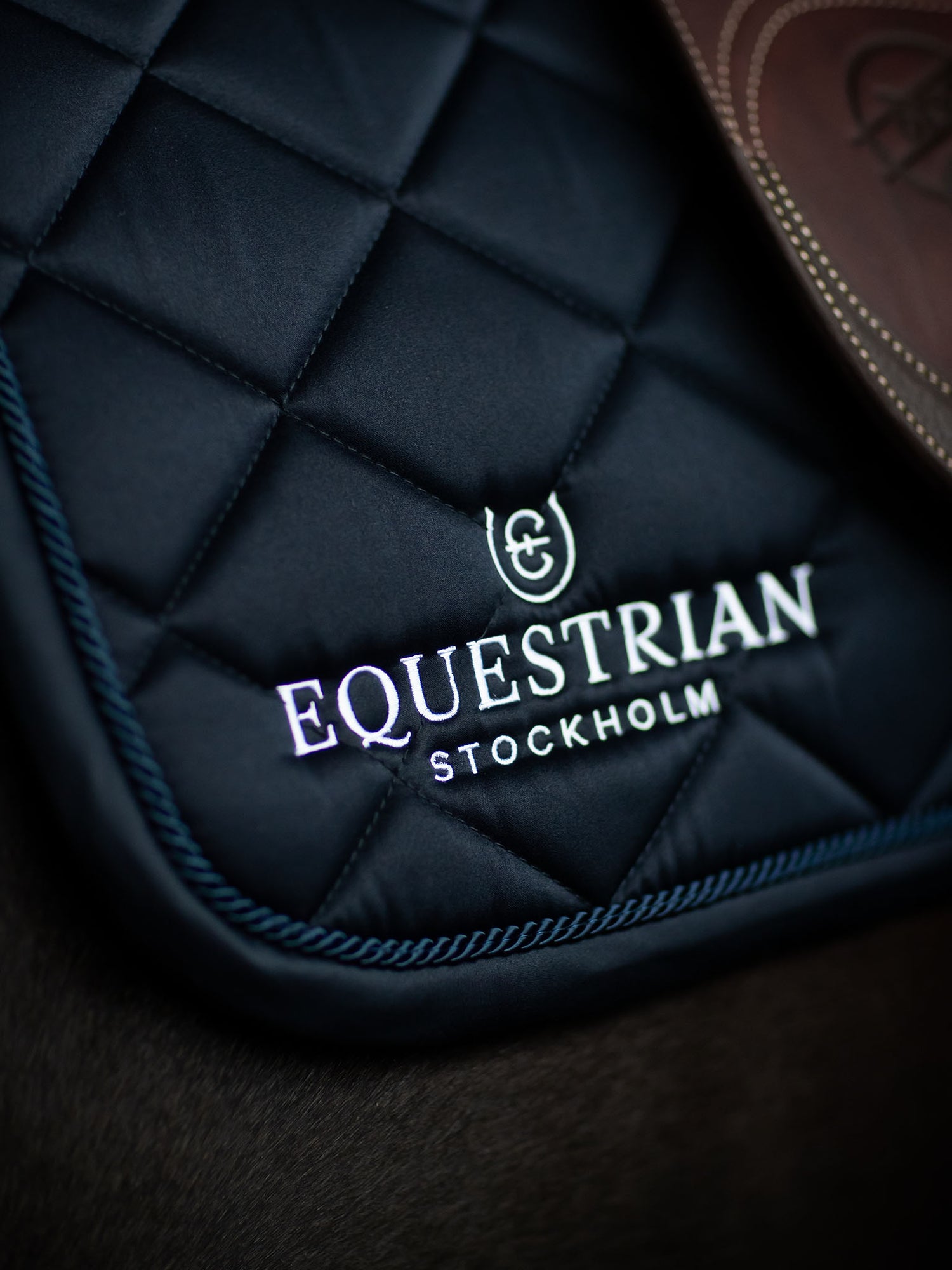 Studio image of Equestrian Stockholm Jump Saddle Pad Line Midnight Blue with white embroidery, navy piping, saddle and horse.
