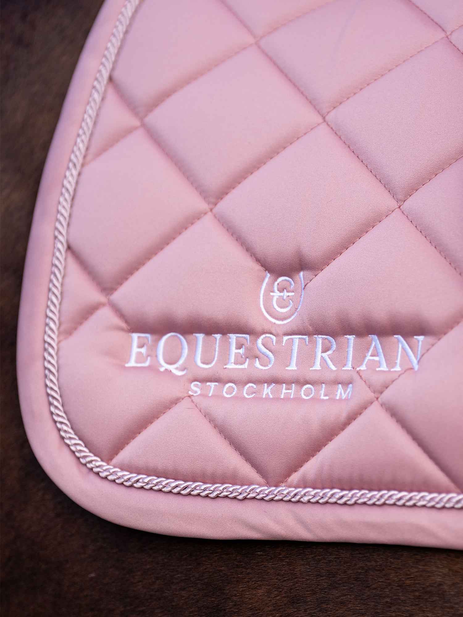 Studio image of Equestrian Stockholm Jump Saddle Pad Line Pink with white embroidered logo and quilted details.