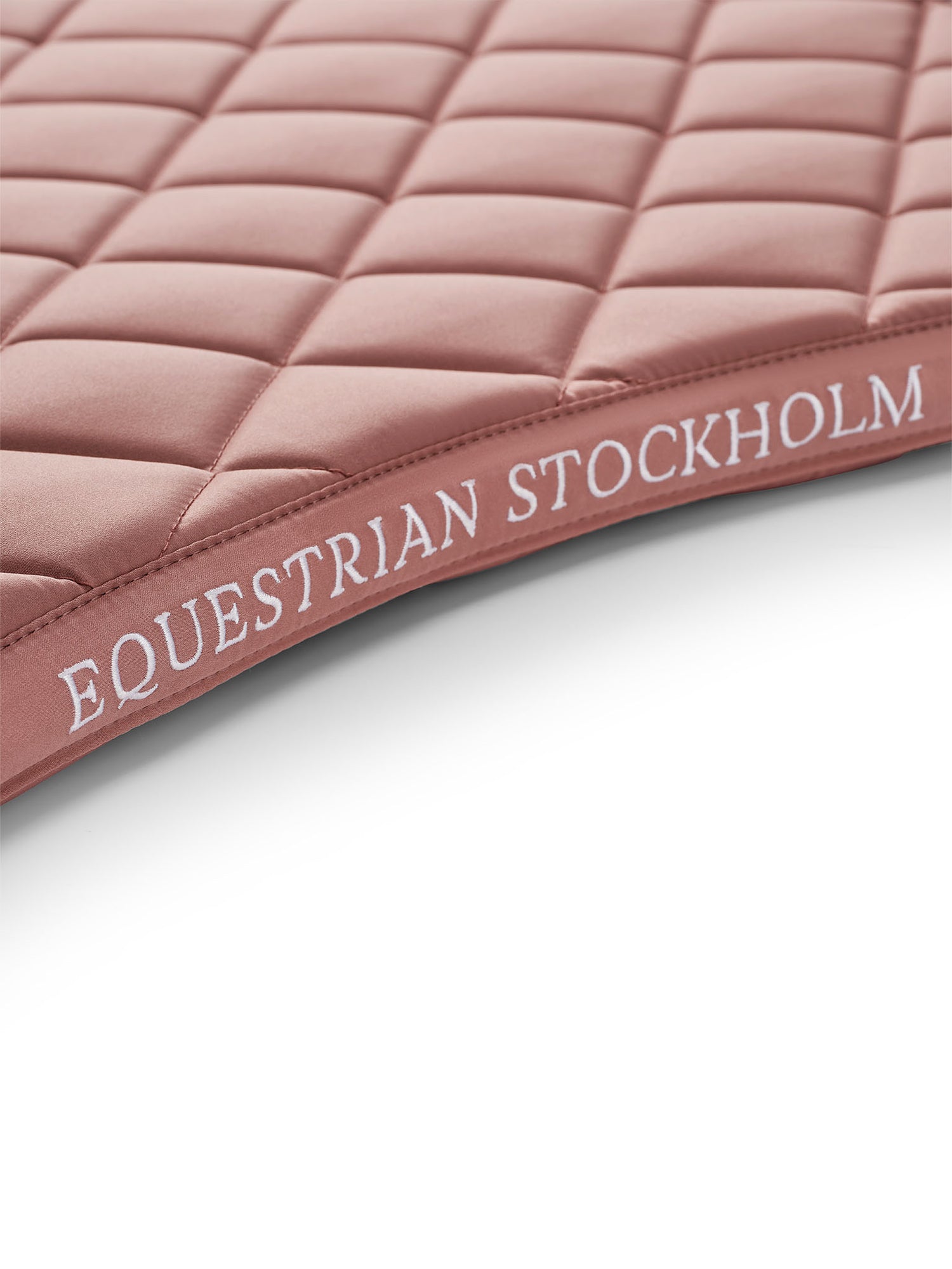 Studiobillede af Equestrian Stockholm Dressurunderlag Line Pink med hvidt broderi og signatur line-quiltning.