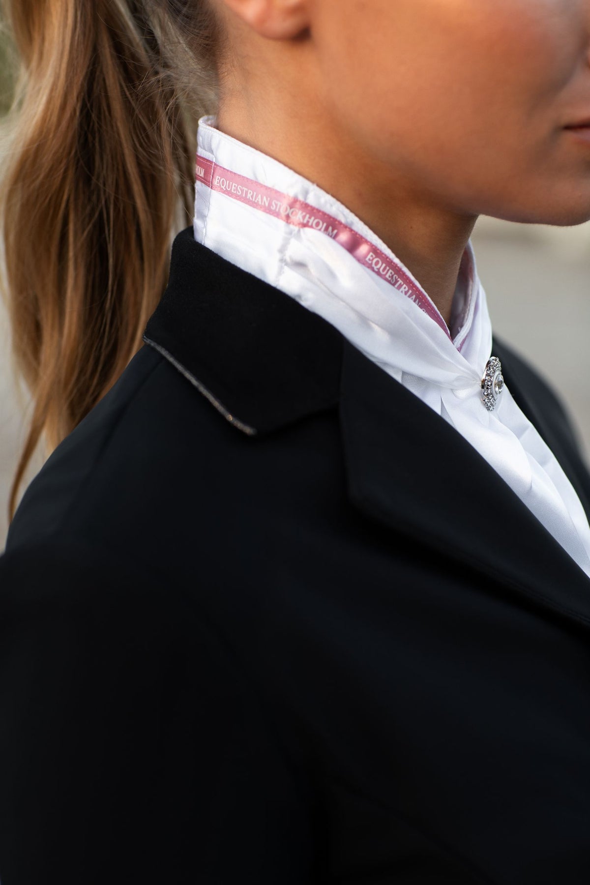 Image studio du Plastron Queen Sportive Pink blanc d'Equestrian Stockholm, liseré satiné rose et cristal, veste noire.