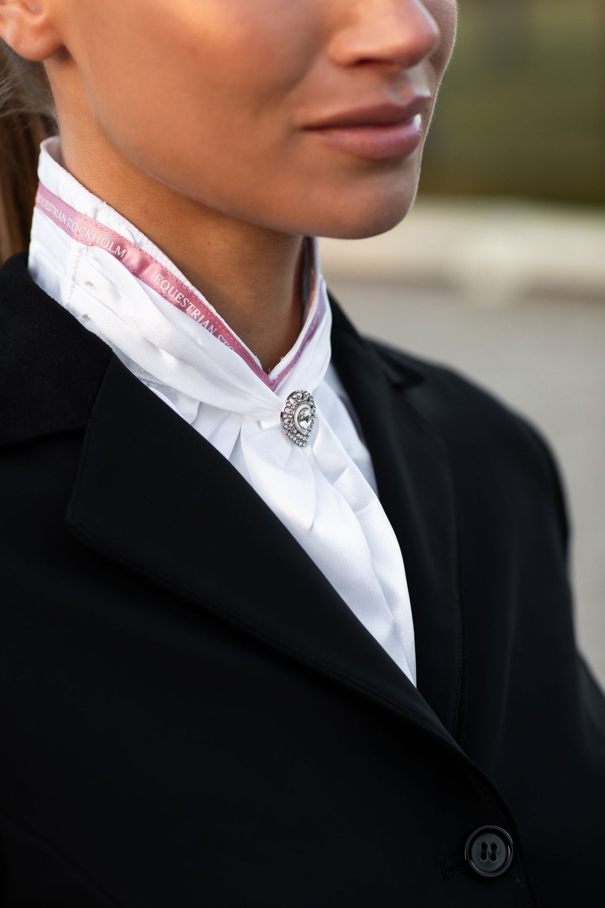 Imagen de estudio de Equestrian Stockholm Corbata de Montar Queen Sportive Pink con ribete rosa y cristal en chaqueta negra.