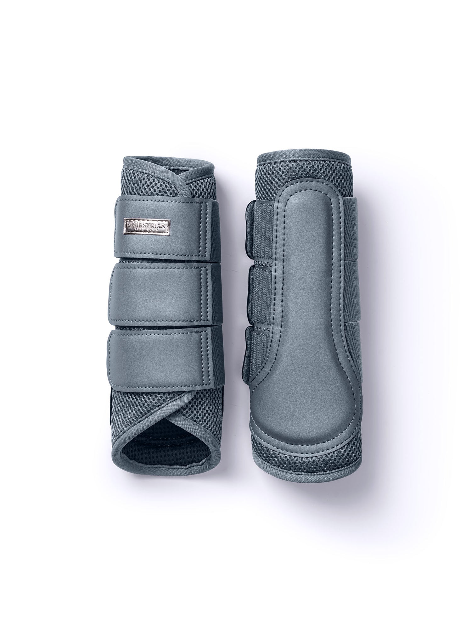 Studio image of a pair of Equestrian Stockholm Metallic Blue Mesh Brushing Boots with 3D mesh and silver badge.