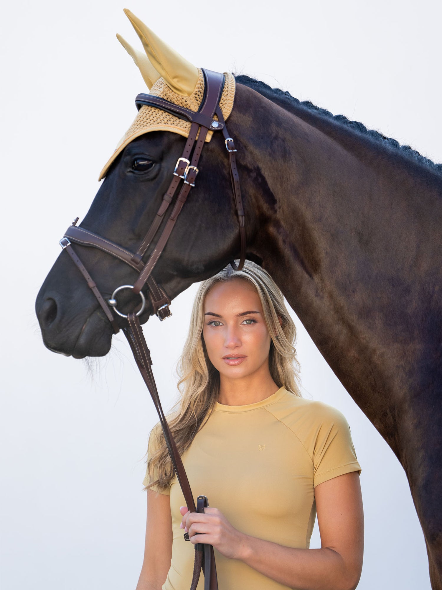Equestrian Stockholm model in a Midsummer Glow base layer beside a horse wearing the matching yellow ear bonnet.