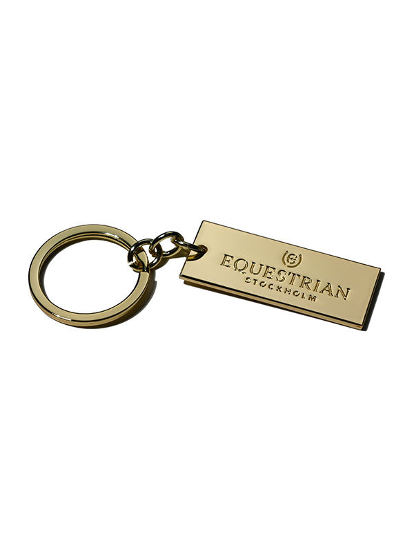 Studio image of Equestrian Stockholm Gold Keychain with an engraved logo on a polished rectangular tag.