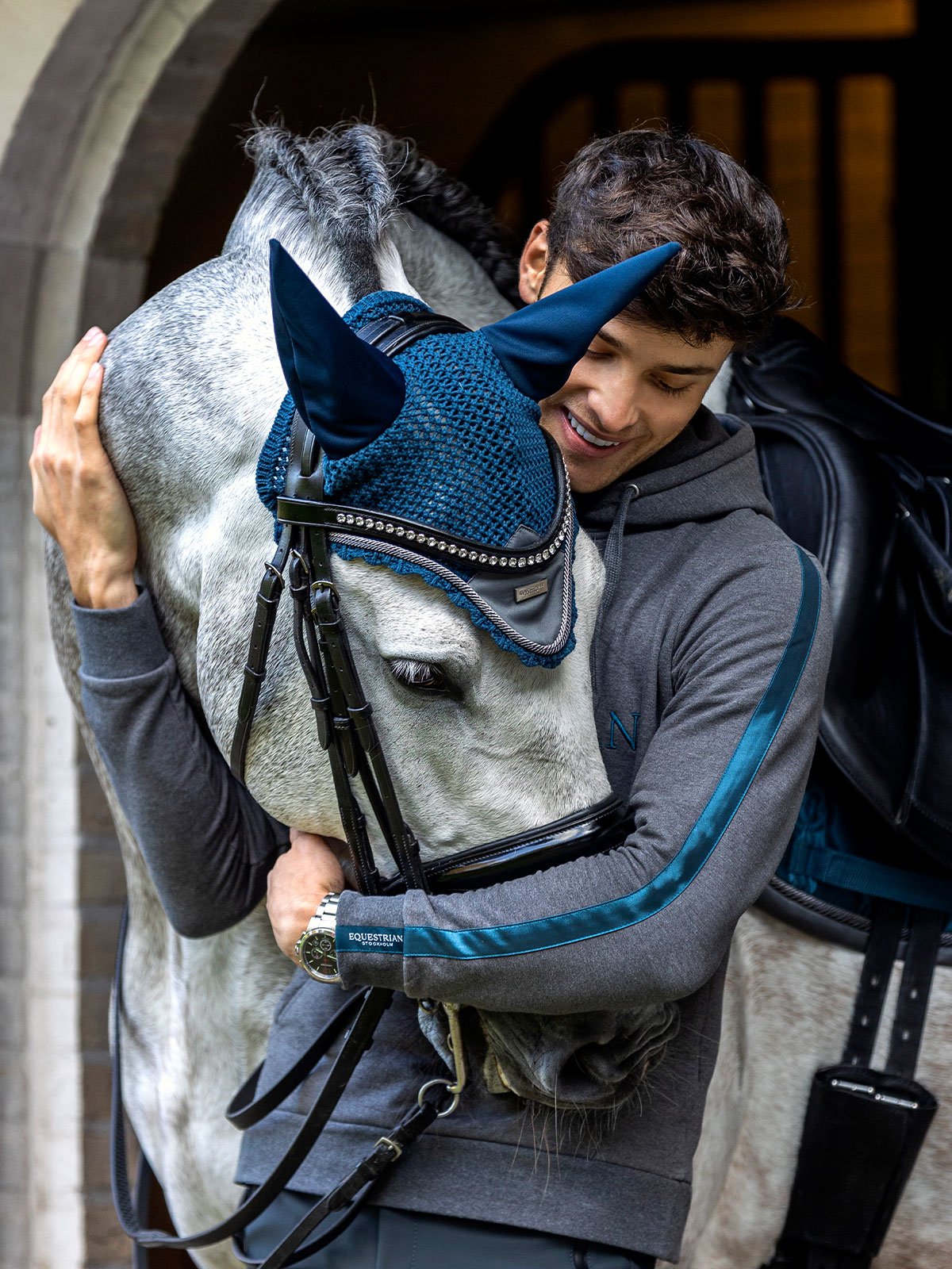 Matt Harnacke hugs a horse wearing the blue and silver Ear Bonnet Matt Harnacke Collection by Equestrian Stockholm.