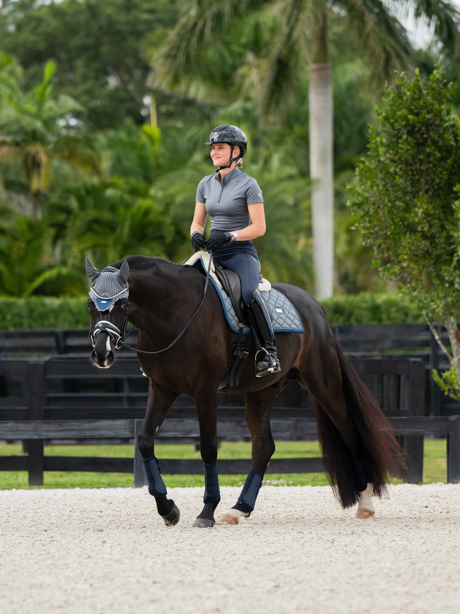 Equestrian Stockholm diamant-quiltet dressurunderlag i metallic blue på mørk hest med rytter, ørehætte og bandager til hest.