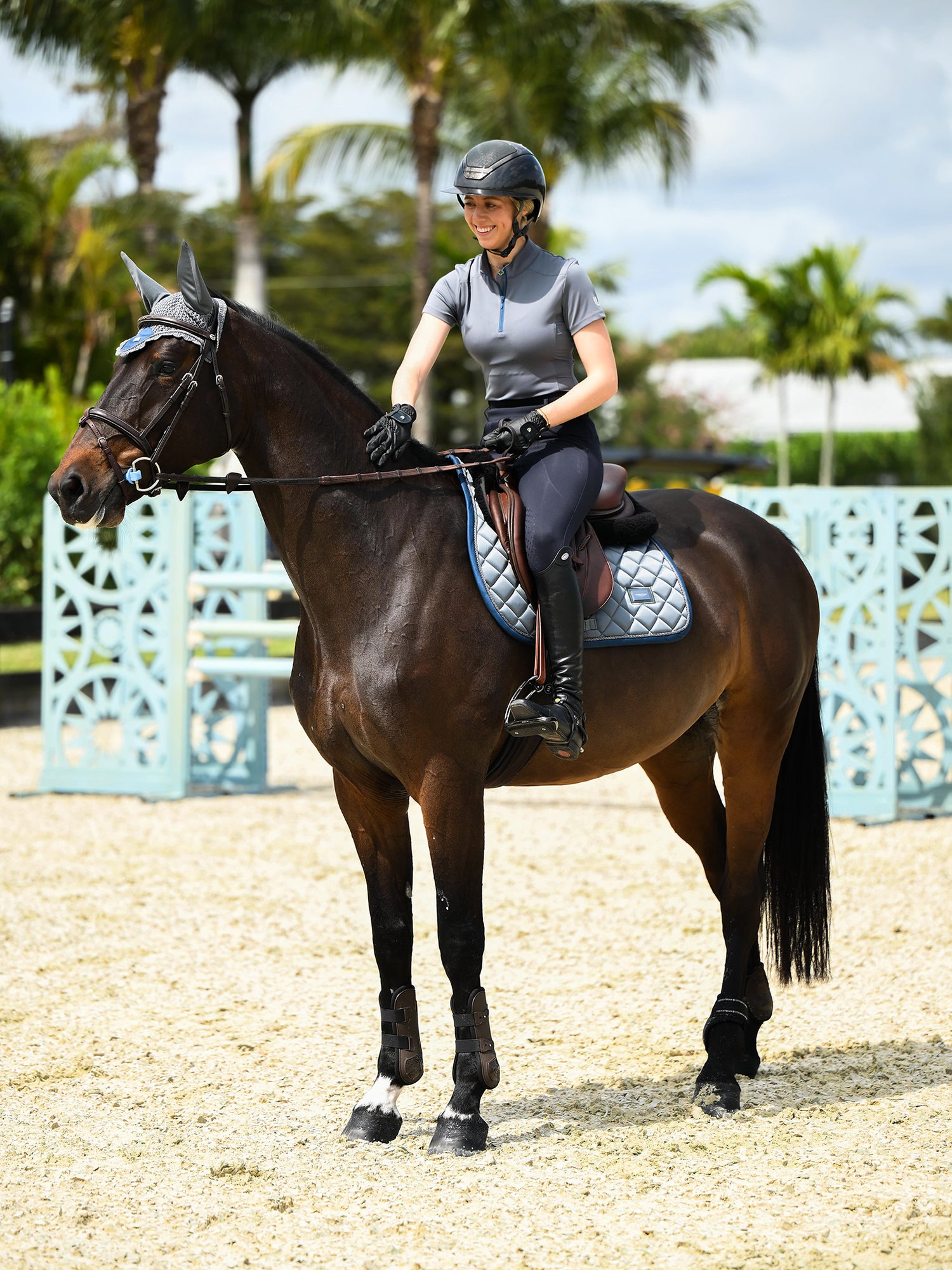 Rytter og hest iført Equestrian Stockholm Springunderlag Metallic Blue, matchende ørehætte og trense på en ridebane.
