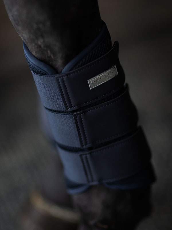Studioaufnahme von Equestrian Stockholm Mesh Gamaschen Midnight Blue mit silbernem Abzeichen an einem Pferdebein.