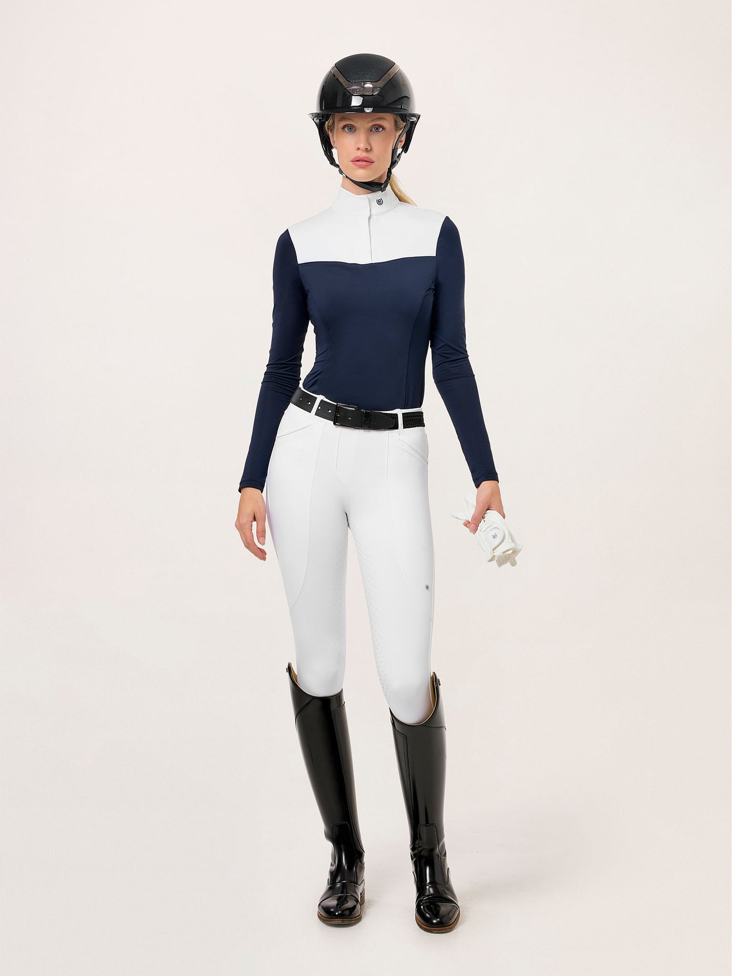 Modelo con Equestrian Stockholm Mallas y Leggings de Montar Premium Blanco, top navy, casco, cinturón, botas y guantes.