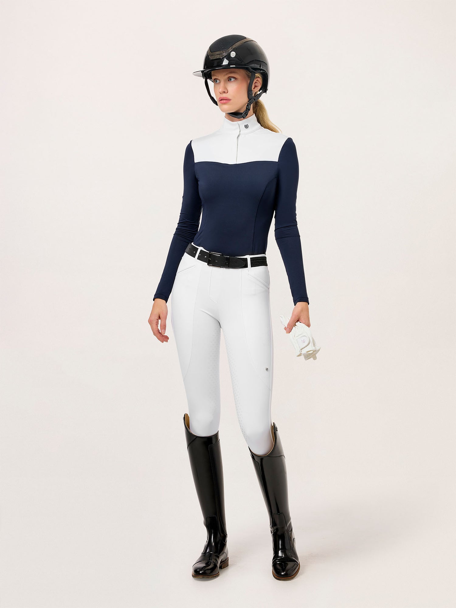 Modelo con Mallas y Leggings de Montar Premium Blanco de Equestrian Stockholm, camisa navy, casco, cinturón, guantes y botas.