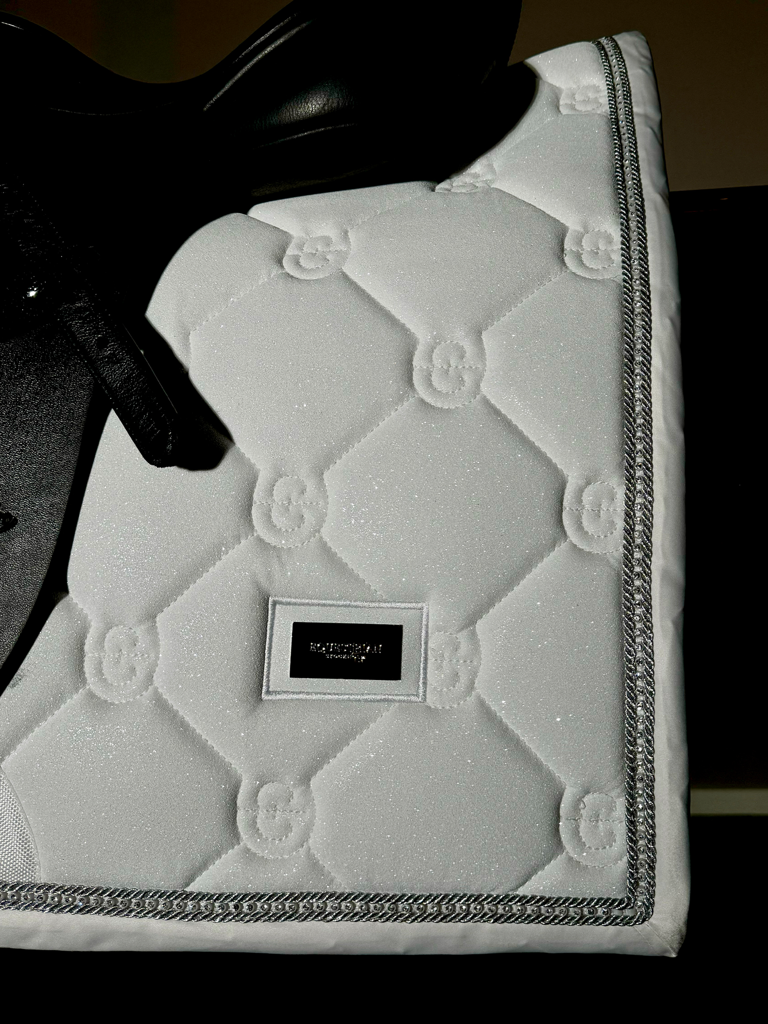 Studio image of Equestrian Stockholm Dressage Saddle Pad Crystal White Glimmer with crystal piping under a black saddle.
