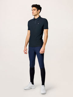 A model wearing Equestrian Stockholm Polo Shirt Zip Men Black, navy breeches, black socks, and white sneakers.