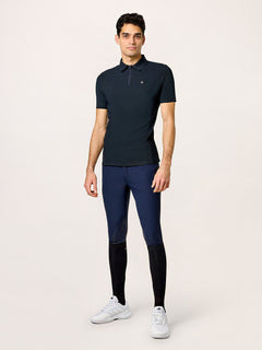 A model wearing Equestrian Stockholm Polo Shirt Zip Men Black with navy breeches and white sneakers.