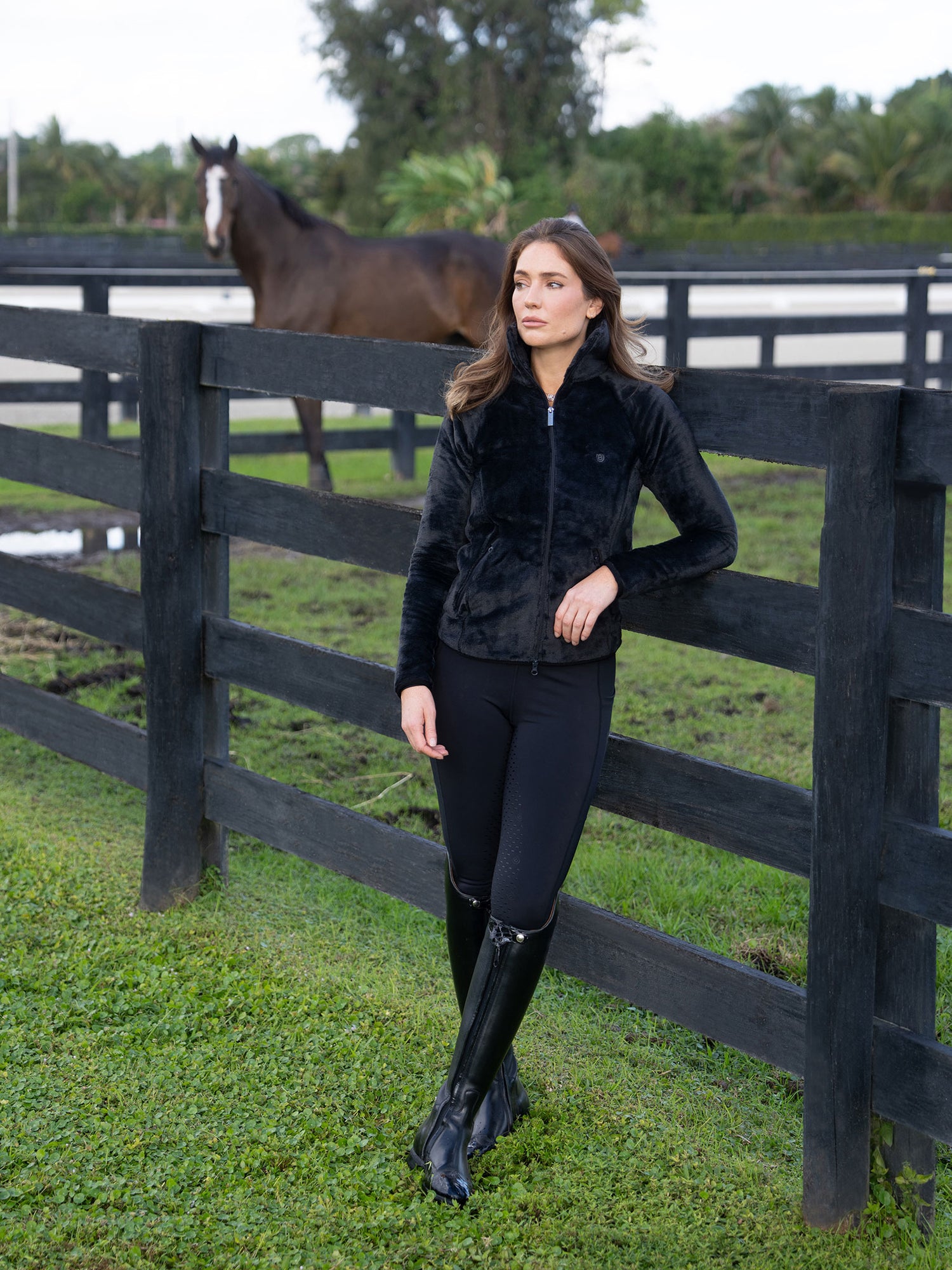 Cavalière en veste polaire Equestrian Stockholm Velvet Black, appuyée contre une clôture avec un cheval.