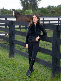 Cavalière en veste polaire Equestrian Stockholm Velvet Black, appuyée contre une clôture avec un cheval.