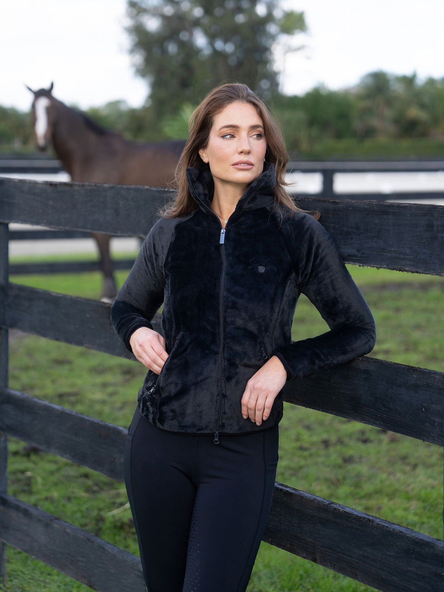 Mannequin portant la Veste Polaire Velvet Black Equestrian Stockholm près d'une clôture avec un cheval.
