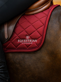 Studiobillede af Equestrian Stockholm springunderlag Line Bordeaux på en brun hest med lædersadel og rytter.