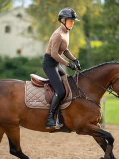 Equestrian Stockholm Springschabracke Line Champagne auf braunem Pferd mit Model in braunem Top und schwarzen Reithosen.