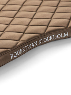 Studioaufnahme der Equestrian Stockholm Springschabracke Line Champagne mit Line-Quilting und weißer Stickerei.