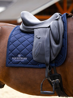 Navy Equestrian Stockholm Dressage Saddle Pad Line Midnight Blue with line quilting and white logo, under a black saddle.