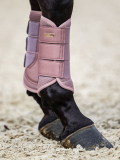 Studioaufnahme der Equestrian Stockholm Mesh Gamaschen Pink mit 3D-Mesh und silbernem Abzeichen an Pferdebeinen im Sand.