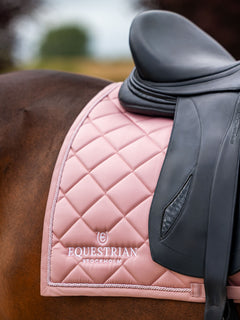 Equestrian Stockholm dressurunderlag i Line Pink med hvidt logobroderi under en sort sadel på en hest.