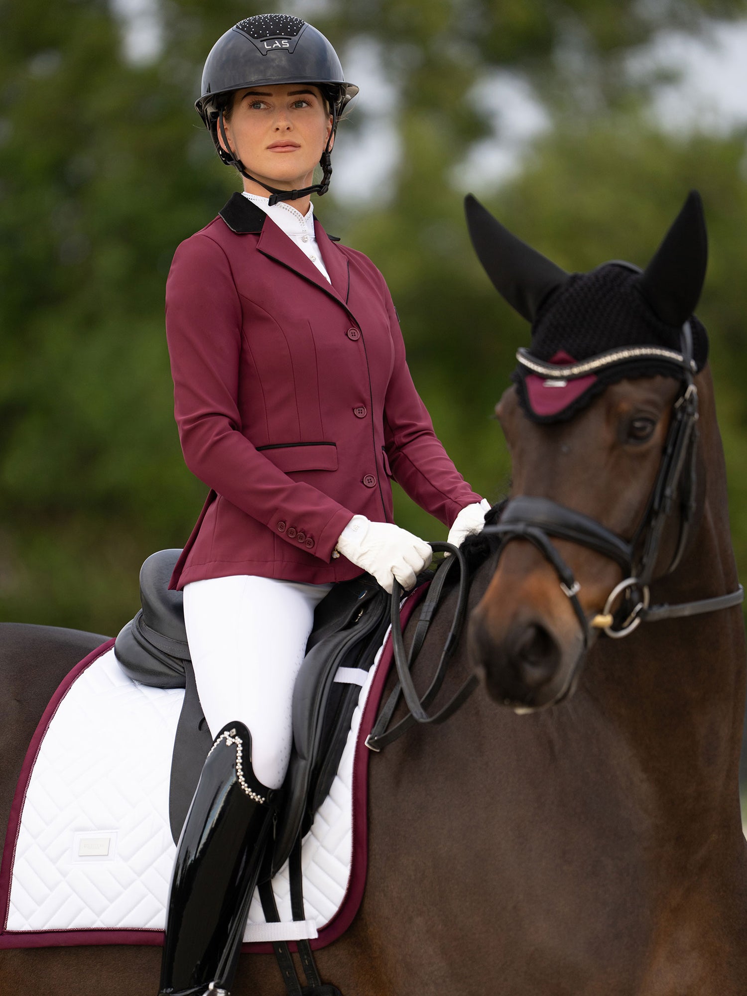 Veste de Concours Classic Merlot Equestrian Stockholm, tapis de dressage blanc et bonnet sur un cheval et sa cavalière.