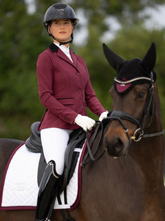 Veste de Concours Classic Merlot Equestrian Stockholm, tapis de dressage blanc et bonnet sur un cheval et sa cavalière.