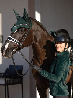 A model wearing Equestrian Stockholm Sycamore Green Velvet Fleece Jacket next to a horse in a matching velvet ear bonnet.
