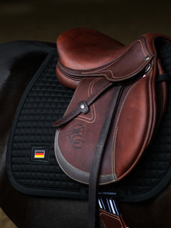 Equestrian Stockholm Jump Saddle Pad Cotton Black Germany logo with square quilting under a brown saddle on a horse.